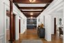 An image of the interior of a 1905 Neoclassical home. The view is from the main entry door and focuses on the entry hall. Features detailed millwork, wood beam ceiling, hardwood floors, and a built-in winebar and cabinetry.