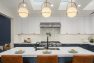 An image of the interior of a 1905 Neoclassical home. Focuses on the spacious chef's kitchen as seen from the kitchen island. Features white subway tile backsplash, a pot-filler fixture above the range, a large gas range, globe pendant lights, and brown leather barstools.