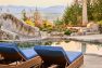 An image of a residential landscape featuring an in-ground pool. Features a sweeping view of forest and mountains in the background. Includes wicker lounge seating, outdoor path lighting, and stone-look