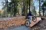 A person riding their bike over a boardwalk in an outdoor bike skills park. Gravel paths connect the boardwalks. — Mercer Island Bike Skills Area – Board & Vellum