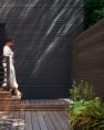 A person in white walks down the exterior stairs at the house, depending toward a wood deck. The house behind the stairs is a charcoal gray. At the end of the stair is a fence.