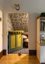 A children’s play room with a shelf on the right and, straight ahead, is a small pony door painted in yellow and green that leads to s little play nook under the house eaves. The play nook has patterned wall paper on the walls and ceiling